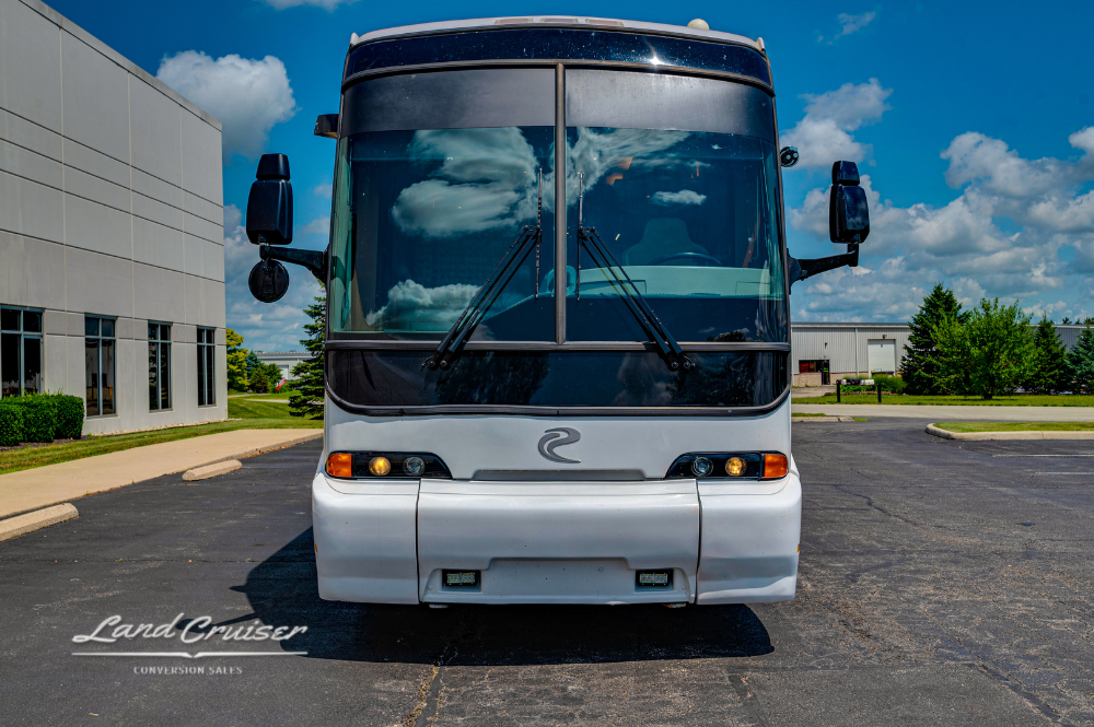 Front view of white MCI motorhome with gold and brown stripes