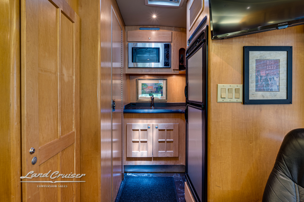 Entryway view into galley with built-in microwave, pantry drawers, and black flooring